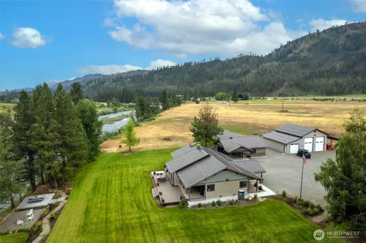 From above, the property reveals its perfect blend of comfort and function: a beautiful craftsman-style home with expansive decking, a large shop/garage for all your needs, and a sprawling lawn bordered by riverfront access and natural beauty.