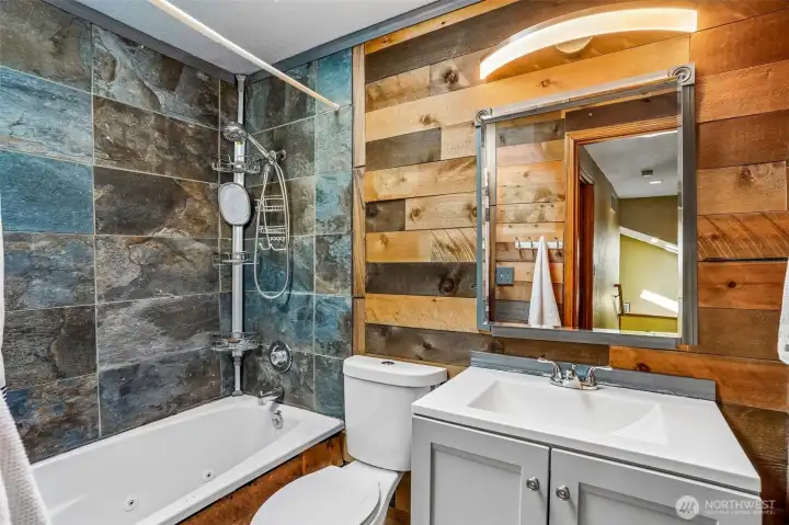 Moody, modern, and full of character ... this beautifully updated bathroom features rich wood accents, striking slate-style tile surround, and a spa-inspired soaking tub that brings warmth and style together perfectly.