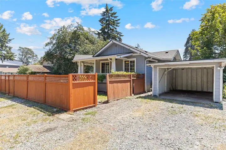 Detached carport is enclosed on three sides and needs only a door to be a full garage.  There are two gates to access the home - the one near the carport is open in this photo to give context, the second is along the left edge of the photo.