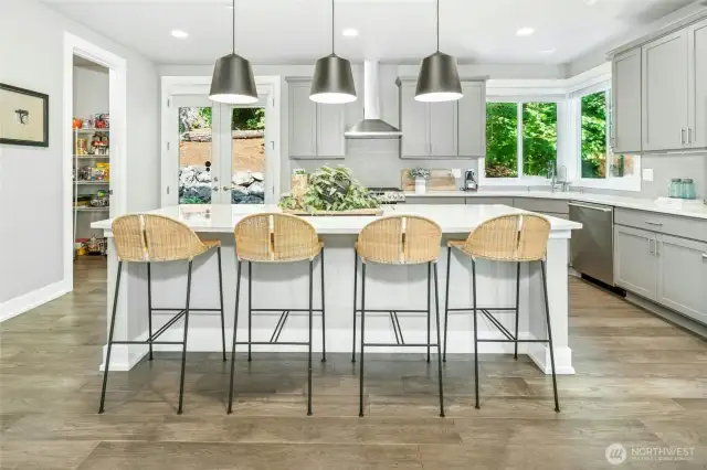 The large gourmet kitchen features quartz countertops, an oversized island with seating, stainless steel appliances, and a walk-in pantry for ample storage.