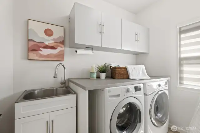 The large laundry room/mudroom located just off the kitchen and adjacent to the attached garage features utility sink, folding table, coat/backpack hooks and ample cabinetry.