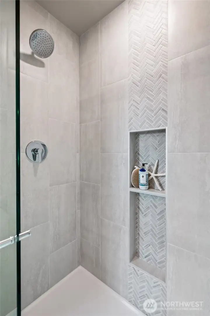 Primary Shower is finished with floor to ceiling title, accent tiles  with convenient in set shelving and glass shower doors.   Photos are of model home in the community.