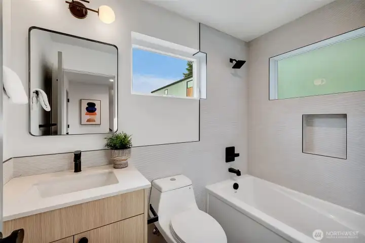Main level full tiled bathroom with a deep soaking tub, custom windows (one with privacy glass), and lighting.