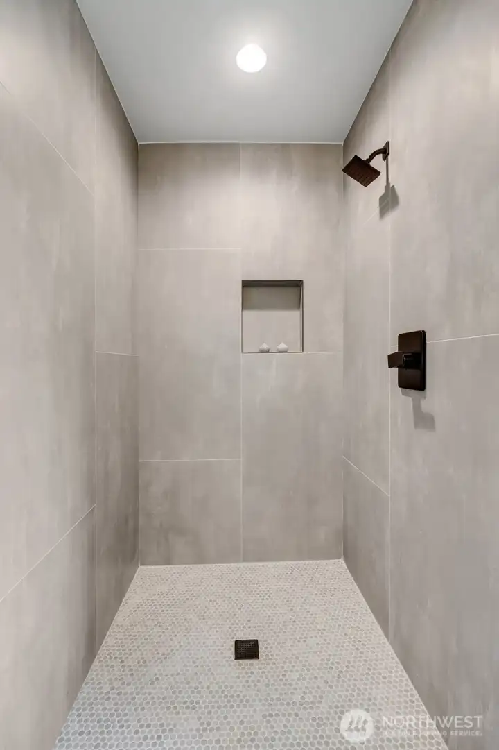 Large walk-in tiled shower with penny tile floor and contrasting fixtures.