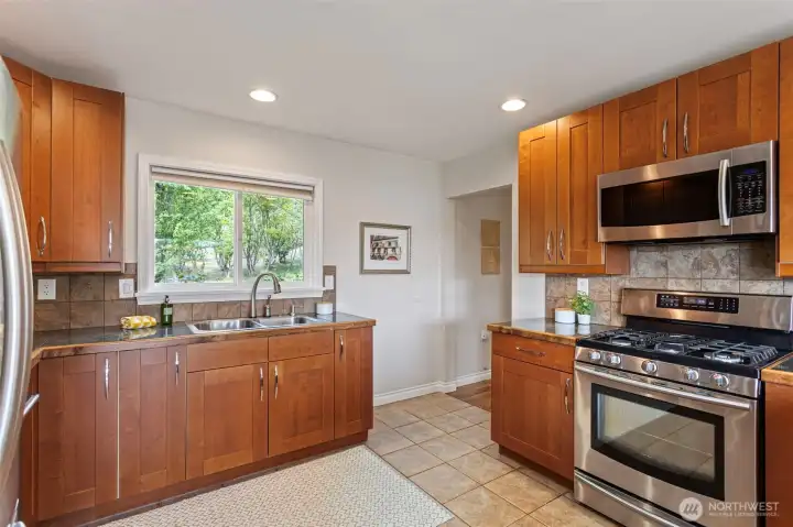 A double stainless sink is situated strategically under the large kitchen, with a touch faucet, tiled backsplash, under-cabinet lighting and stainless appliances.