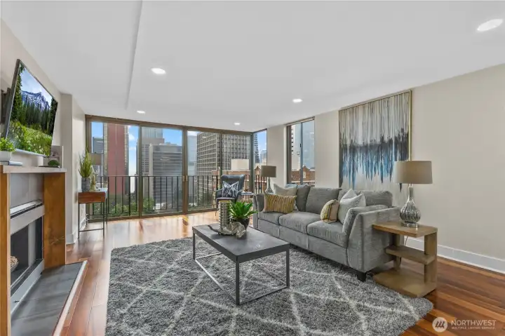 Sunlit living room with floor-to-ceiling windows, cozy fireplace, and sweeping city and water views.