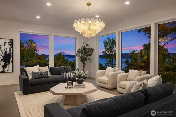 Gather in a living room wrapped in floor-to-ceiling views, where the glow of a cascading chandelier meets vivid sunsets over Lake Washington and Mount Rainier