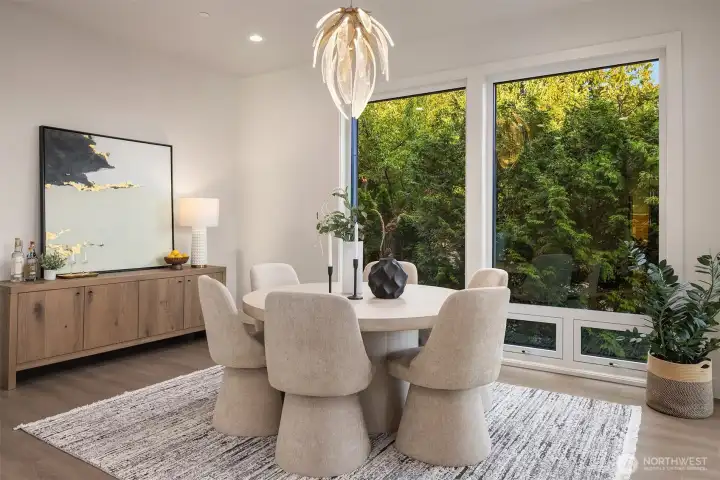 A cozy dining nook bathed in natural light, where floor-to-ceiling windows frame a lush, private green backdrop (not shown-the slider opening on to the main floor entertaining deck)