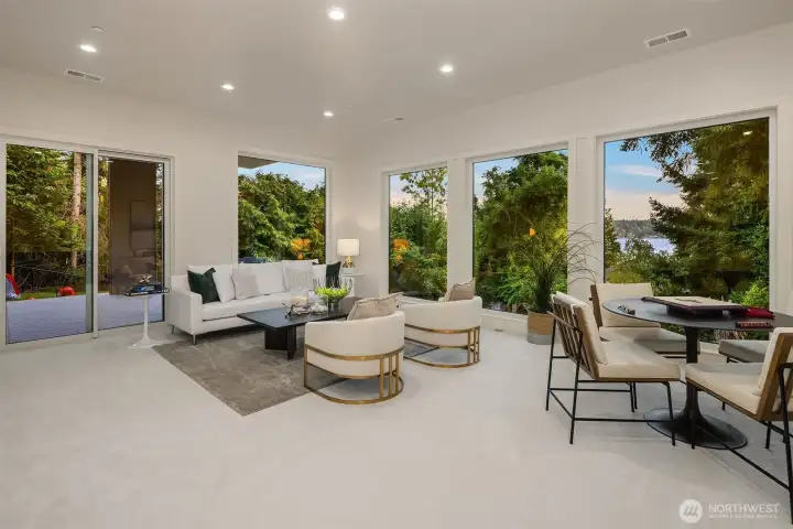Light-filled lower-level rec/game room with wall-to-wall windows, indoor-outdoor flow, and tranquil tree-lined and lake views + sliders that open onto the covered entertaining deck