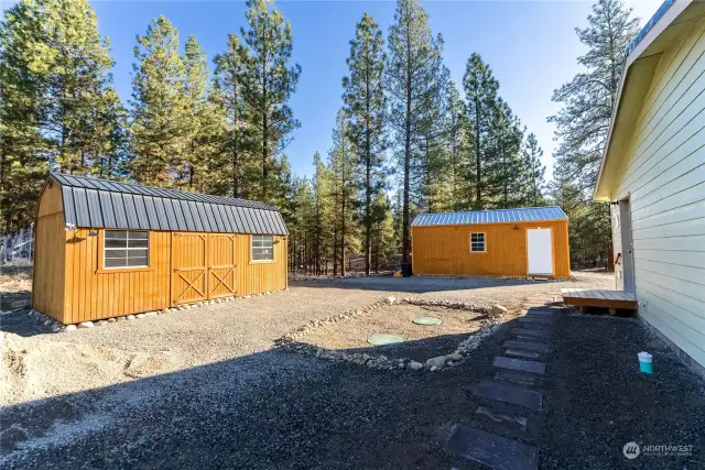 Outbuildings to North and East of Home. Solar powered motion sensor system at storage shed. Storage shed has 2 Lofts and workbench. Single car garage detached from home has 2 windows, man door and garage door.