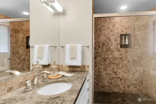 Natural finishes grace this primary 3/4 bath with style: travertine tiled shower, limestone counter tops the custom vanity with infinity sink and newer hardware and the limestone floor offers radiant heat. Perfect!