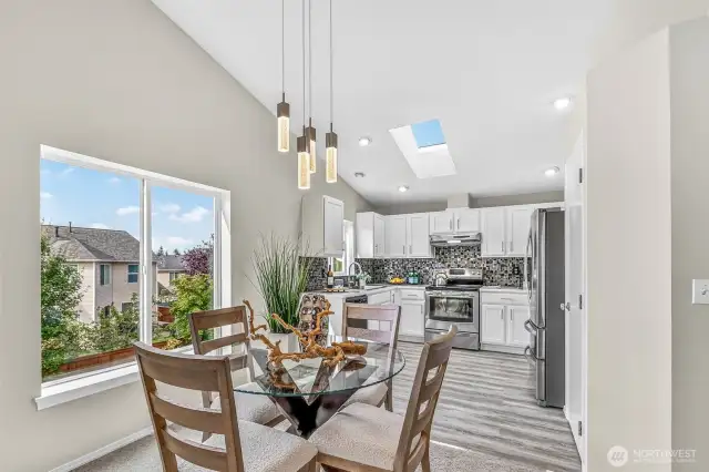 The dining area sits by an expansive window with treetop outlooks, accented by modern pendant lighting. New luxury vinyl plank extends from here into the kitchen, while the open sightlines keep everyone connected.