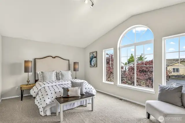 The spacious vaulted-ceiling bedroom at the front of the home enjoys a striking arched window and abundant natural light. Soft new carpet and neutral tones create a serene retreat with flexible layout options.