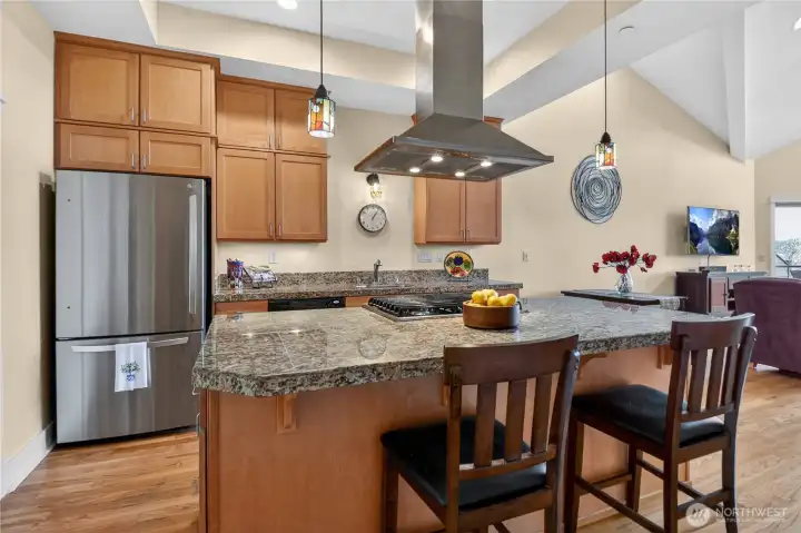 The chef’s kitchen features stainless steel appliances, a spacious island, and a stainless steel hood positioned above the island cooktop, offering both functionality and a refined, professional-grade design.