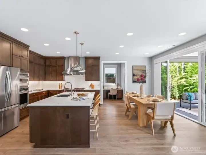 At the heart of the home is the chef’s kitchen, beautifully appointed with high-end Huntwood cabinetry, commercial-grade appliances including a Wolf range, an oversized center island, quartz countertops, a large walk-in pantry, abundant storage, and a convenient tech zone.