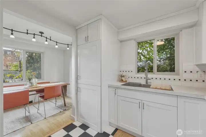 Fresh white cabinetry, updated counters, and a sleek sink make this bright kitchen both functional and stylish, with views to the lush courtyard greenery.