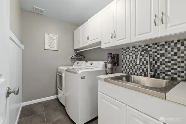 The laundry room has plenty of cabinet storage space and a utility sink.