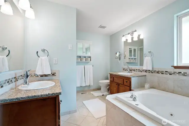 Primary ensuite bathroom with view of the seperate sink vanities with granite counter tops and stunning tile throughout as well as the seperate soaking tub.