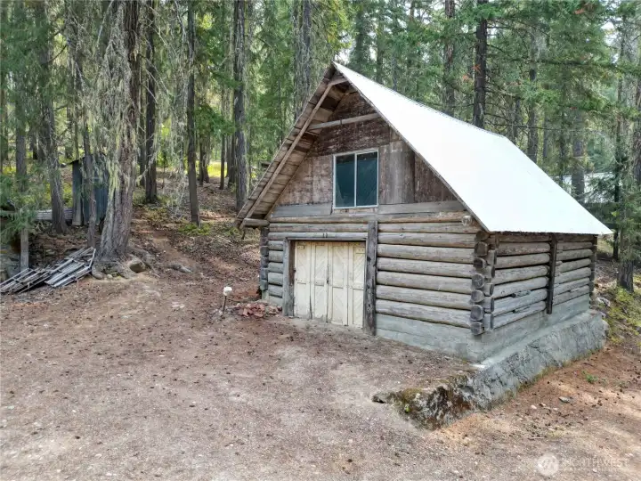 Rustic detached log garage with upper-level space, set among the evergreens for added utility and charm.