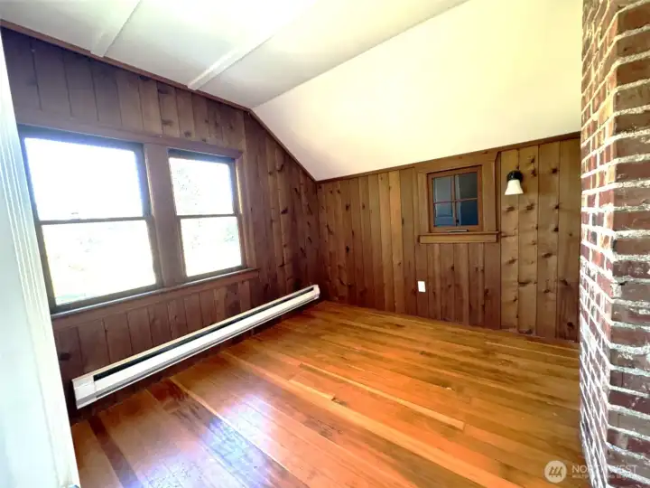 Upstairs bedroom 1 featuring hardwood floors, real wood wall coverings, and large windows for ample natural light.