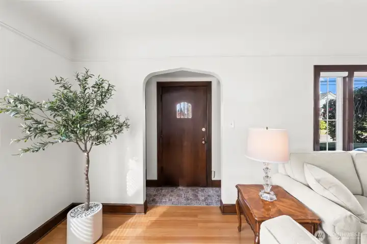 Entryway: Step through the original arched doorway into a bright, welcoming foyer. The space features beautiful hardwood floors and a glimpse of the architectural character found throughout the home.