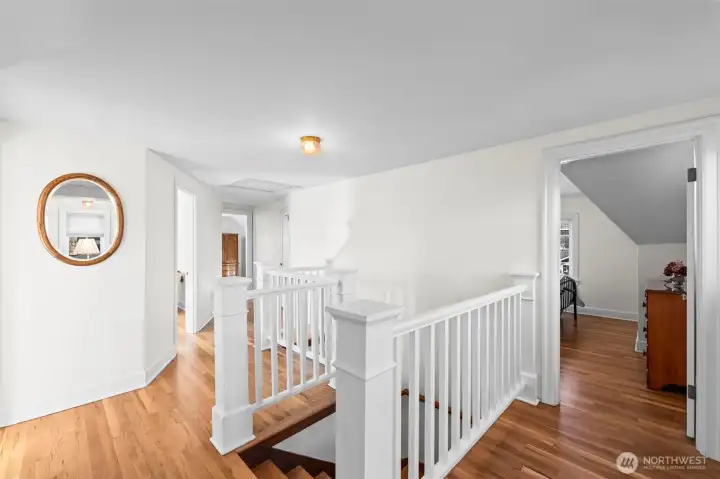 Oak Hardwood Landing: The upstairs landing showcases continuous oak hardwood flooring and a classic white banister, leading to the private upper-level quarters in an open, airy layout.