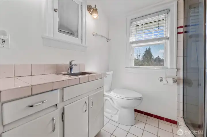 Upstairs Bathroom: This three-quarter bath combines vintage appeal with modern utility. It features a classic pink tile countertop, a charming built-in medicine cabinet, and a bright window that keeps the space feeling fresh.