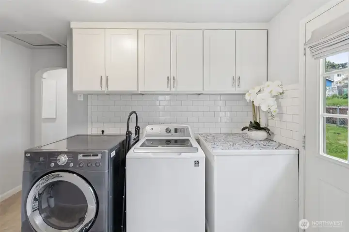 Updated laundry room with washer and dryer, cabinetry, and bright natural light.