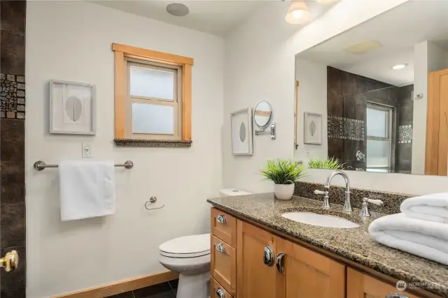 Spacious main floor bathroom with ample vanity, natural stone counters and a large walk-in shower.
