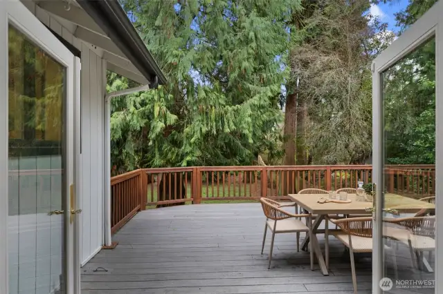 French doors lead to the spacious deck, overlooking the tranquil backyard, where mature cedar trees provide natural shade, creating an inviting outdoor retreat.