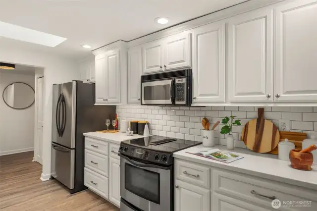 This bright and inviting galley-style kitchen offers an abundance of cabinetry for storage, sleek stainless steel appliances, and a French door refrigerator with a bottom freezer. The cheerful white cabinetry and subway tile backsplash create a fresh and timeless look.