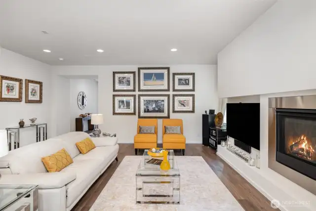 Open living room features sleek fireplace, wide-planked flooring, mirroring windows and recessing lighting.
