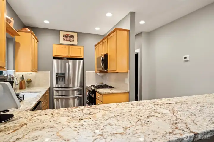 The effortless flow of the hardwood floors moves into the dining room and kitchen area which features slab granite, warm wood toned cabinetry, tiled backsplash, breakfast bar seating and stainless steel appliances including a new dishwasher, 4 drawer/door refrigerator, gas stove and pantry.