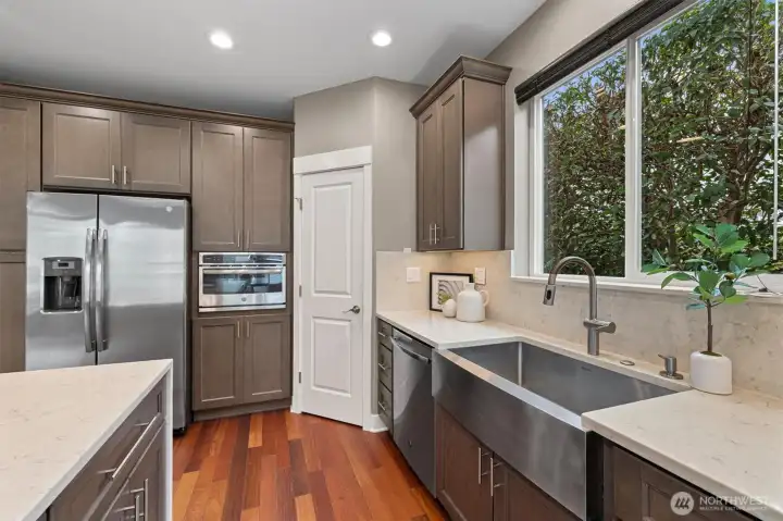 Designer kitchen with expansive quartz island and sightline to generous-sized pantry, offering both style and exceptional storage for everyday living.