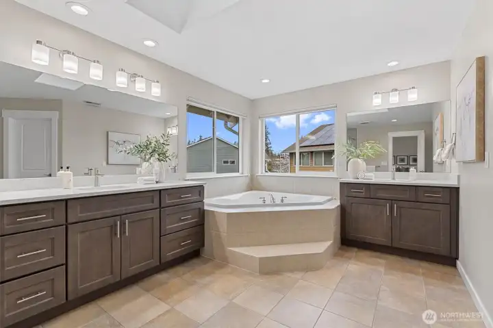 Spa-inspired primary bathroom with quartz countertops, dual vanities, soaking tub, glass shower, skylights, and walk-in closet access.