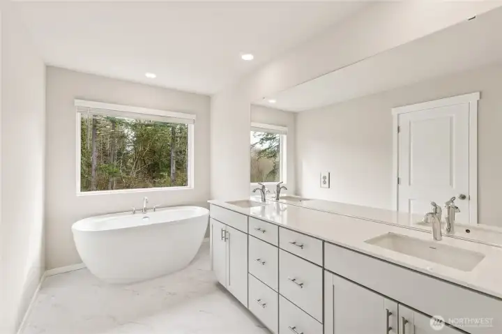 Luxurious primary en-suite bathroom featuring a freestanding soaking tub beneath a large window. Photos are representative only and may display different color package and/or upgrades.