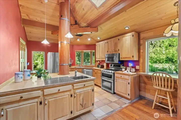 Warm and inviting kitchen with natural wood cabinetry, center island with prep sink, and stainless steel appliances. Vaulted wood ceilings and expansive windows bring in abundant natural light. Warm and inviting kitchen with natural wood cabinetry, center island with prep sink, and stainless steel appliances. Vaulted wood ceilings and expansive windows bring in abundant natural light.
