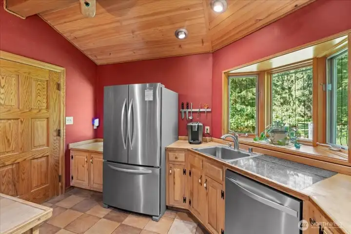Kitchen featuring stainless steel appliances, wood cabinetry, and large corner windows with views of the surrounding landscape. Functional workspace includes generous counter space and tile flooring. Kitchen featuring stainless steel appliances, wood cabinetry, and large corner windows with views of the surrounding landscape. Functional workspace includes generous counter space and tile flooring.