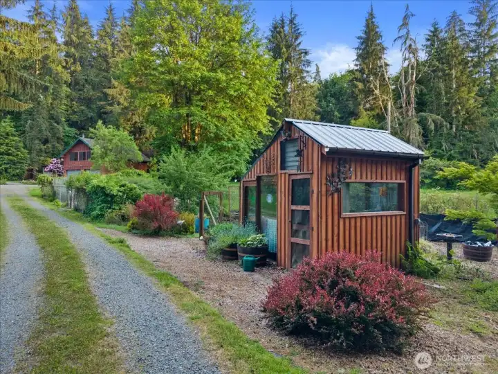 Charming detached garden shed with surrounding planting beds and gravel pathway set within a peaceful forested setting. Landscaped grounds offer space for gardening and outdoor enjoyment. Charming detached garden shed with surrounding planting beds and gravel pathway set within a peaceful forested setting. Landscaped grounds offer space for gardening and outdoor enjoyment.