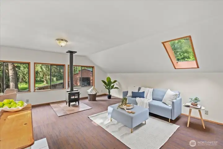 Cozy loft living area features skylights, large windows, and a freestanding stove with surrounding views of the property. Cozy loft living area features skylights, large windows, and a freestanding stove with surrounding views of the property.