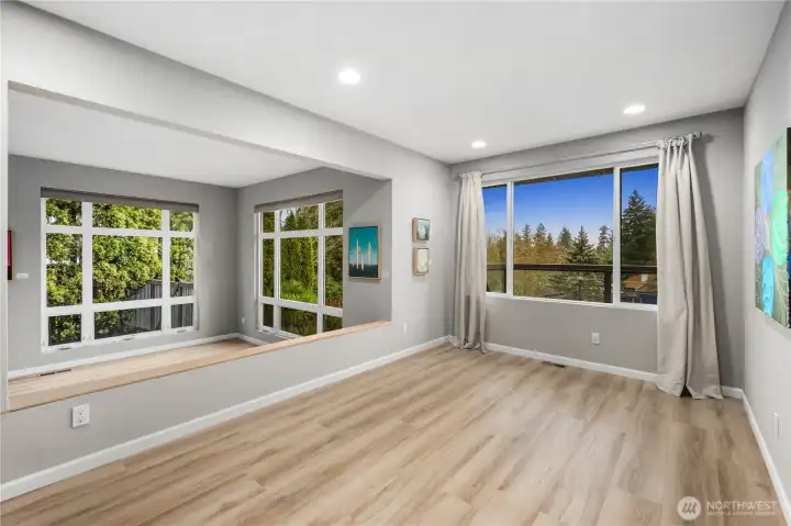 Light-filled living and dining space features wide windows, gray freshly painted tones, recessed lighting, and warm wood floors opening to tranquil views.