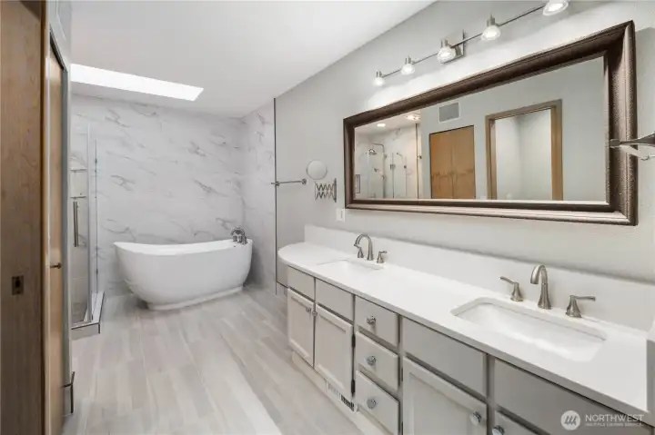 Elegant primary bathroom featuring dual vanities, quartz counters, framed mirror, freestanding soaking tub, marble-style finishes, and refined spa-like ambiance.Fully remodeled