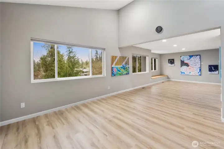 Bright, expansive primary bedroom space with elegant new flooring, ample  windows, art-lined walls, high ceilings, and flexible layout for  expansive living on the top floor of this home.