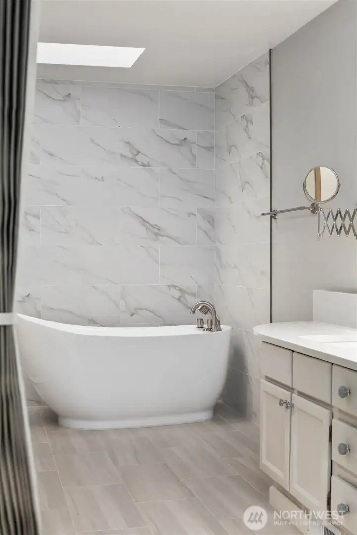 Spa-inspired bathroom with freestanding soaking tub, marble-style tile surround, modern vanity, soft lighting, and serene contemporary finishes.