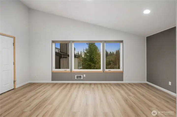 Bright bedroom featuring wide plank floors, large windows overlooking greenery, neutral tones, recessed lighting, and peaceful, airy atmosphere.
