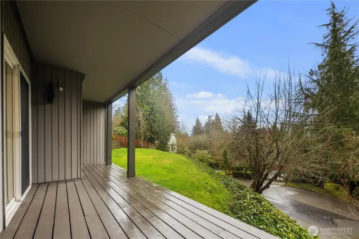 Covered outdoor deck overlooking lush grounds and trees, offering peaceful privacy, fresh air, and an inviting extension of living space.
