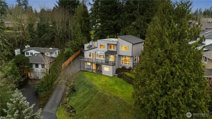 Elevated modern home nestled among evergreens, offering privacy, terraced landscaping, hillside setting, and glowing interiors framed by serene natural surroundings. Easterly views of  Cascade mountains year round.