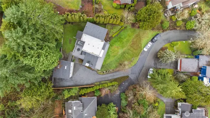 Aerial view showcasing private hillside home, winding driveway, lush landscaping, and generous grounds nestled within a quiet residential enclave.