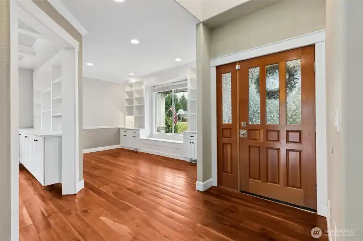 This entry foyer makes a strong first impression. Gorgeous cherry hardwood floors anchor the space, paired with a wood front door featuring a privacy glass panel that brings in light without putting your life on display. From here, you can see straight into the den or formal parlor space and into the formal dining room, which gives the whole entry a sense of openness and flow. Muslin toned walls, wide white trim, and high ceilings keep everything feeling bright, warm, and welcoming the moment you walk in.  there is 1/2 bath right around the corner too.