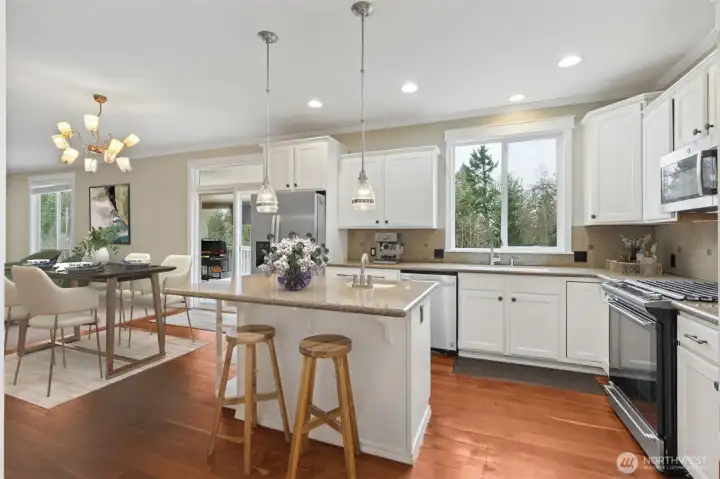 This kitchen checks a lot of boxes with white shaker cabinetry and granite slab counters keeping the look fresh and classic, while the island offers seating and a second prep sink that actually makes a difference when more than one person is cooking. Pendant lights add a little personality overhead, cherry hardwood floors ground the space, and stainless steel appliances including a 5-burner rang are all included. With a large window over the sink and a sliding glass door opening to the casual dining area, this kitchen feels bright, connected, and very livable.